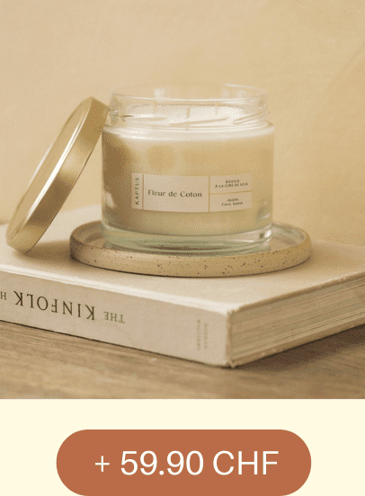 Une bougie parfumée en pot en verre, étiquetée « Fleur de Coton », posée sur un livre intitulé « The Kinfolk Home ». Prix affiché : + 59.90 CHF.