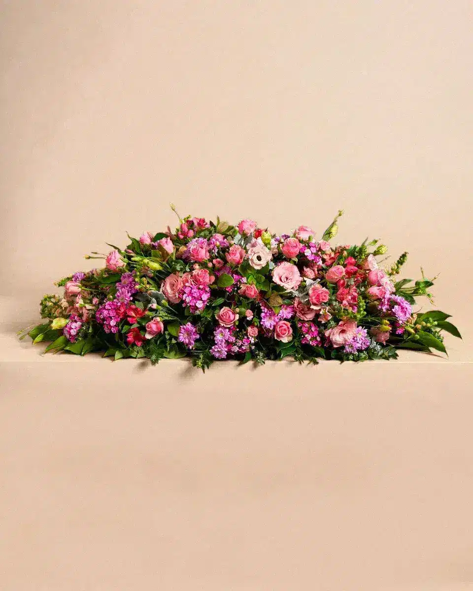 Livraison gerbe de fleur : Un bouquet de fleurs composé de roses et de fleurs violettes repose élégamment sur une surface beige, mettant en valeur son arrangement soigné et coloré.