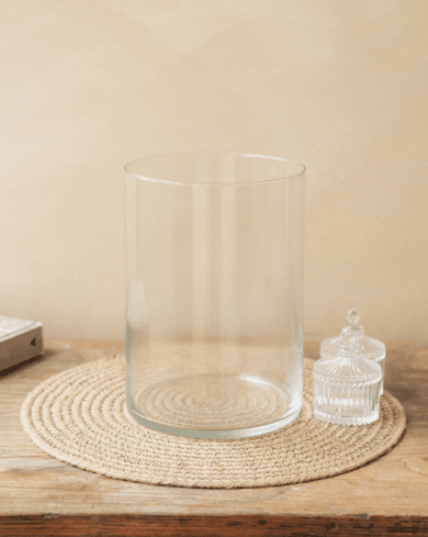 Vase en verre et un bocal en cristal sur un napperon en corde tressée sur une table en bois. Contexte de fond beige.