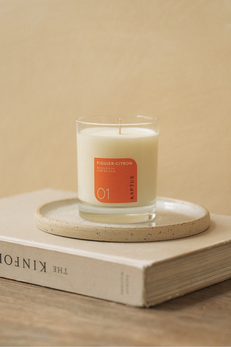 Bougie figuier-citron allongée sur une assiette posée sur un livre intitulé “The Kinfolk”. Étiquette :